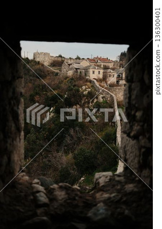 Ancient stone wall of Pocitelj Fortress leading toward historic houses on a hilltop, surrounded by wild vegetation and autumn colors in Bosnia Ancient stone wall of Pocitelj Fortress leading toward historic houses on a hilltop, surrounded by wild vegetation and autumn colors in Bosnia 136300401