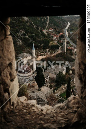 View through a stone window inside Pocitelj Fortress overlooking an old mosque with dome and minaret, surrounded by historic stone houses and autumn hills in Bosnia View through a stone window inside Pocitelj Fortress overlooking an old mosque with dome and minaret, surrounded by historic stone houses and autumn hills in Bosnia 136300405