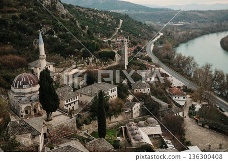 High angle view of Pocitelj village mosque and stone tower beside the Neretva River, surrounded by trees and historic buildings in a quiet Balkan landscape High angle view of Pocitelj village mosque and stone tower beside the Neretva River, surrounded by trees and historic buildings in a quiet Balkan landscape 136300408