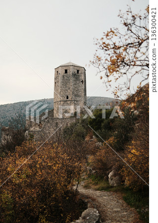 Stone tower of Pocitelj Fortress rising above autumn vegetation and rocky paths, highlighting medieval defensive architecture in the Neretva River valley 136300421