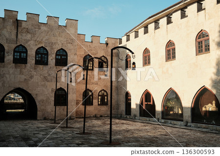 Stone courtyard with medieval style buildings and lanterns in Andricgrad, Visegrad, Bosnia and Herzegovina. Calm historic space with geometric forms, shadows and cultural atmosphere Stone courtyard with medieval style buildings and lanterns in Andricgrad, Visegrad, Bosnia and Herzegovina. Calm historic space with geometric forms, shadows and cultural atmosphere 136300593