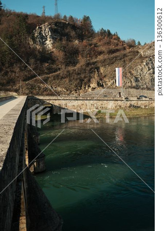 Stone arches of Mehmed Pasha Sokolovic Bridge rise above the green waters of the Drina River in Visegrad. Strong geometry and textures highlight historic engineering Stone arches of Mehmed Pasha Sokolovic Bridge rise above the green waters of the Drina River in Visegrad. Strong geometry and textures highlight historic engineering 136300612