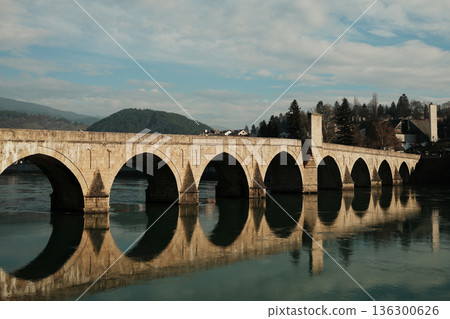 Historic Mehmed Pasha Sokolovic Bridge spans the Drina River in Visegrad, Bosnia and Herzegovina. Stone arches and soft reflections highlight the calm atmosphere of this iconic landmark Historic Mehmed Pasha Sokolovic Bridge spans the Drina River in Visegrad, Bosnia and Herzegovina. Stone arches and soft reflections highlight the calm atmosphere of this iconic landmark 136300626