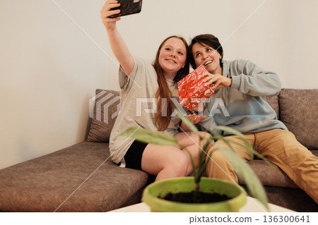 Two friends take a cheerful selfie together while holding a decorated gift box. The concept reflects happiness, celebration and shared friendship moments Two friends take a cheerful selfie together while holding a decorated gift box. The concept reflects happiness, celebration and shared friendship moments 136300641