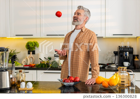 Middle-aged man bites fresh apple in kitchen for healthy diet snack smiling satisfied home kitchen 136300828