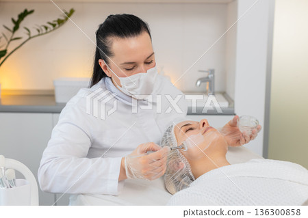 Enzyme therapy beautician applying moisturizing medical cream on young adult woman face with brushes 136300858