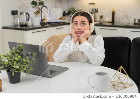 Young woman in headphones thinking with laptop leans on hands worried decision responsibility mind Young woman in headphones thinking with laptop leans on hands worried decision responsibility mind 136300904