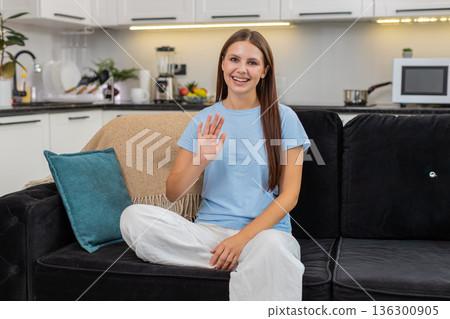 Young woman waves hello looks to camera friendly greet warm welcome smile kind eye contact and joy Young woman waves hello looks to camera friendly greet warm welcome smile kind eye contact and joy 136300905