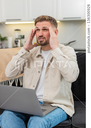 Young man with laptop suffers headache rubs temples closes eyes takes breath long break relief calm 136300926