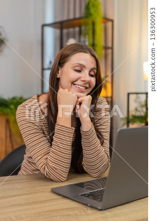 Young woman looks at laptop screen watches online travel advert leans on hands dreams about vacation Young woman looks at laptop screen watches online travel advert leans on hands dreams about vacation 136300953