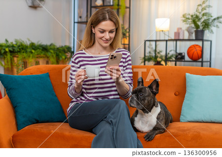 Middle-aged woman with dog enjoys morning coffee and reads news on smartphone relaxed mood indoors Middle-aged woman with dog enjoys morning coffee and reads news on smartphone relaxed mood indoors 136300956