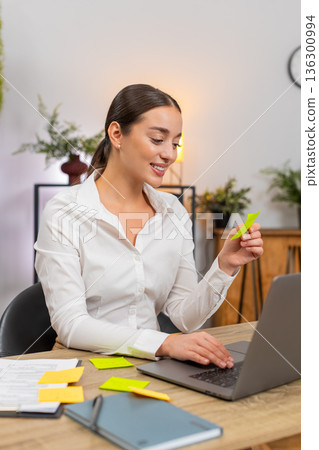 Young businesswoman opens laptop lays stickers and starts first task from list with confident focus 136300994