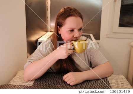 A woman drinks coffee from a yellow cup at the kitchen table, enjoying a calm morning moment. Morning routine concept A woman drinks coffee from a yellow cup at the kitchen table, enjoying a calm morning moment. Morning routine concept 136301429