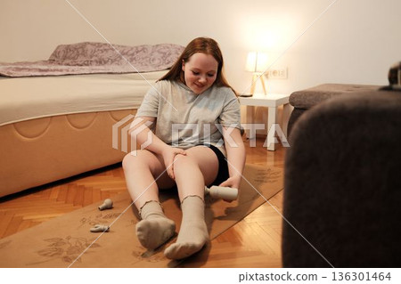 A woman uses a handheld massage device on her leg while sitting on a yoga mat, focusing on recovery and relaxation after exercise A woman uses a handheld massage device on her leg while sitting on a yoga mat, focusing on recovery and relaxation after exercise 136301464