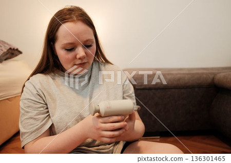 A woman inspects a handheld massage device, calmly preparing for a wellness and relaxation moment at home A woman inspects a handheld massage device, calmly preparing for a wellness and relaxation moment at home 136301465