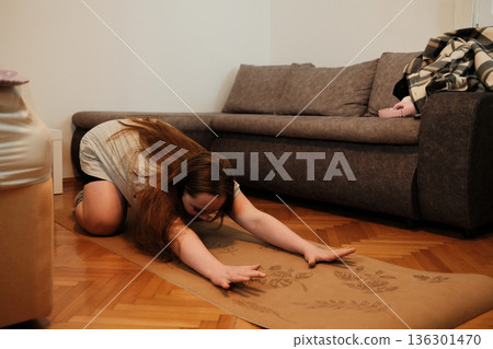 A woman stretches forward on a yoga mat in a child s pose, creating a calm moment of relaxation and flexibility during her home routine A woman stretches forward on a yoga mat in a child s pose, creating a calm moment of relaxation and flexibility during her home routine 136301470