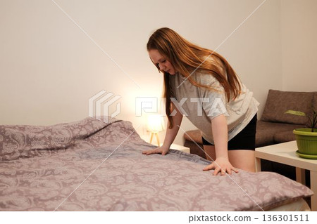 A woman smooths the blanket while making her bed, creating a sense of cleanliness and morning routine in a cozy bedroom A woman smooths the blanket while making her bed, creating a sense of cleanliness and morning routine in a cozy bedroom 136301511