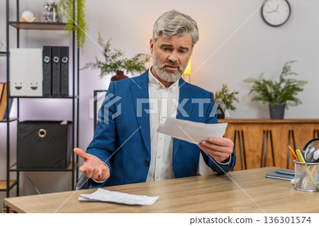Middle-aged businessman stressed by unpaid bills tosses them aside frustrated over budgetary worries Middle-aged businessman stressed by unpaid bills tosses them aside frustrated over budgetary worries 136301574