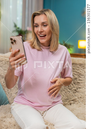 Pregnant woman celebrating baby news texting on smartphone making victory sign smiling super indoors Pregnant woman celebrating baby news texting on smartphone making victory sign smiling super indoors 136301577