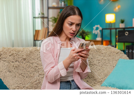 Young woman angrily texting on smartphone waving hand frustrated by chat messages and visible dismay Young woman angrily texting on smartphone waving hand frustrated by chat messages and visible dismay 136301614