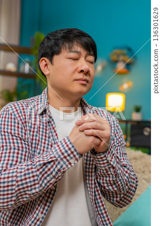 Asian man with eyes closed repeating mantra, calm meditative prayer, hopeful quiet spiritual moment Asian man with eyes closed repeating mantra, calm meditative prayer, hopeful quiet spiritual moment 136301629