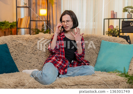 Woman arguing on smartphone at home waving hand with frustration, showing angry facial expression 136301749