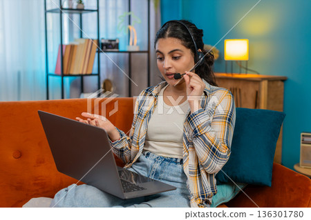 Indian woman call-center operator working home on laptop wearing headset microphone concentrated Indian woman call-center operator working home on laptop wearing headset microphone concentrated 136301780