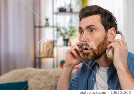 Man in headphones suddenly takes them off looking surprised reacting to strange unexpected sound Man in headphones suddenly takes them off looking surprised reacting to strange unexpected sound 136301800