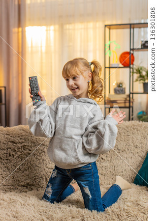 Young teenager girl watching cartoons at home sofa playful dancing, remote in hand fun TV hop energy Young teenager girl watching cartoons at home sofa playful dancing, remote in hand fun TV hop energy 136301808
