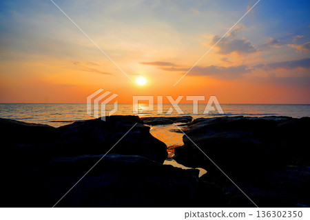 Sunset sea in coastal. Waves at rocks shore. Sunset over calm ocean water with stone rocks 136302350