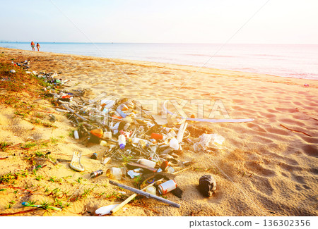 Trash on beach. People walk on sunset at sea. Garbage dump at ocean. Trash, debris on sea beach. 136302356