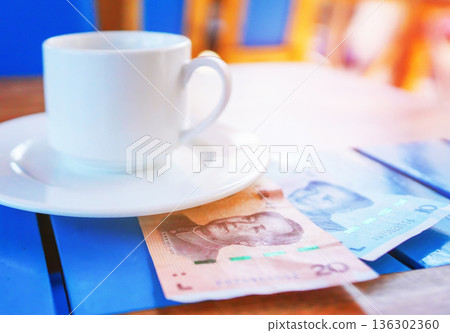Coffee cup on table with yuan bill money in cafe. Payment coffee drink on breakfast. Yuan biill Coffee cup on table with yuan bill money in cafe. Payment coffee drink on breakfast. Yuan biill 136302360