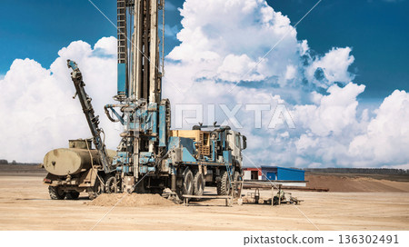 Drilling rig works on the ground to access oil and gas resources under clear skies with clouds in the background during daytime Drilling rig works on the ground to access oil and gas resources under clear skies with clouds in the background during daytime 136302491