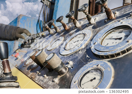 A worker is adjusting the control panel of a drilling rig. Gauges display pressure and depth measurements in an oil extraction site 136302495