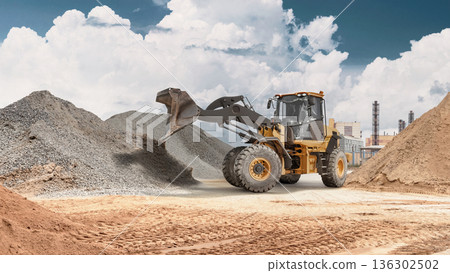 A powerful wheel loader transports sand with a bucket at a construction site. Dust and materials surround the loader as it works on the project A powerful wheel loader transports sand with a bucket at a construction site. Dust and materials surround the loader as it works on the project 136302502
