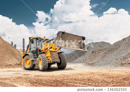 Wheel loader is working at a construction site by transporting sand in a storage bucket for earthworks and bulk handling tasks under a clear sky Wheel loader is working at a construction site by transporting sand in a storage bucket for earthworks and bulk handling tasks under a clear sky 136302503