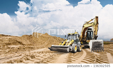 Heavy machinery makes deep tracks in sandy ground at a construction site. A large pile of sand rises in the background under a cloudy sky 136302505