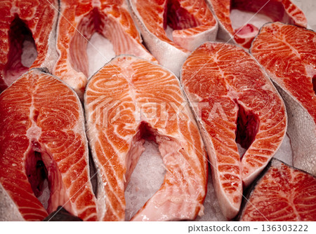 Fresh raw salmon steaks on display, bright orange fish meat with marble texture and skin, ready for cooking, seafood market background. 136303222