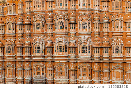 Detailed view of the pink sandstone facade of Hawa Mahal in Jaipur, India, with repeating arched windows and intricate lattice decoration. 136303228