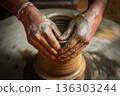 Skilled artisan hands shaping wet clay on a spinning potter wheel, creating a ceramic vase in a traditional pottery workshop. 136303244
