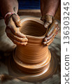 Skilled artisan hands shaping wet clay on a spinning potter wheel, creating a ceramic vase in a traditional pottery workshop. 136303245