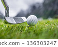Golf club and ball on wet green field with mountains in background. 136303247