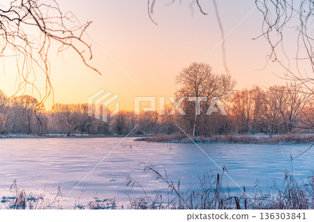 Tranquil frozen winter lake landscape. Warm sunlight on idyllic nature trees Tranquil frozen winter lake landscape. Warm sunlight on idyllic nature trees 136303841