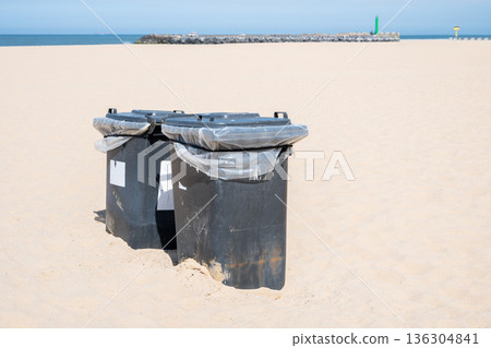Green and black plastic waste containers buried in yellow sand on the beach. Ostend, Belgien. 136304841