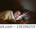 young woman uses smartphone at night while lying in bed 136306259