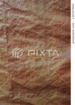 Detailed texture of brownish orange woven tarp fabric with creases and dense plastic fibers Detailed texture of brownish orange woven tarp fabric with creases and dense plastic fibers 136307683