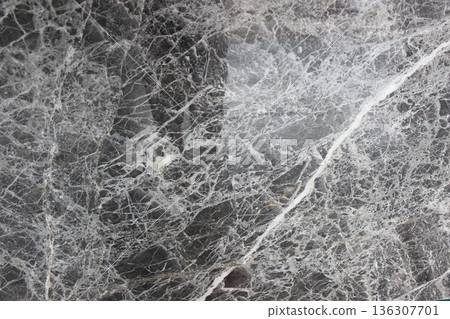Pietra Grey marble texture from Iran with fine white veins crisscrossing over a dark gray background. 136307701