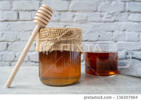 Honey jar with honeycomb, cap of tee and wood spoon stay on the table near napkin. 136307864