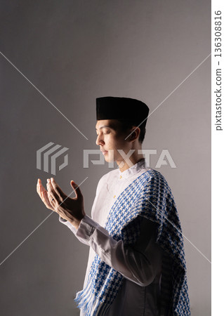 Young individual silently prays within plain studio environment 136308816