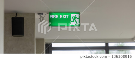 Green emergency exit sign showing the way to escape. Fire exit in the building. Green emergency exit sign showing the way to escape. Fire exit in the building. 136308916